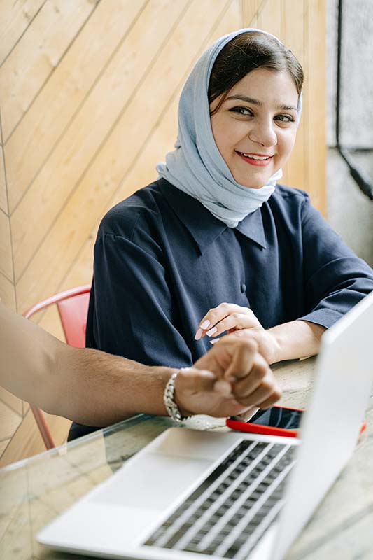 Young girl studying and writing on paper while being tutored over an online meeting